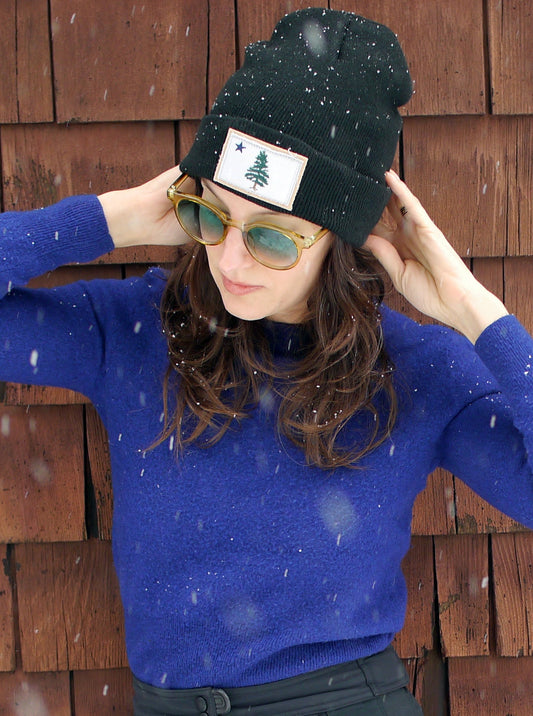 Women wearing an black knit beanie hat with 1901 Original Maine Flag patch appliqué.